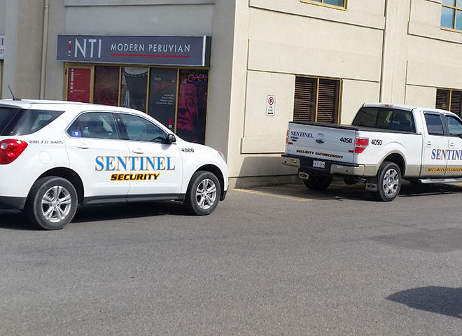 two sentinel security vehicles parked, one white car and one white truck