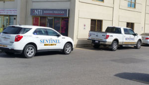 one white sentinel security car and truck parked parallel in parking lot